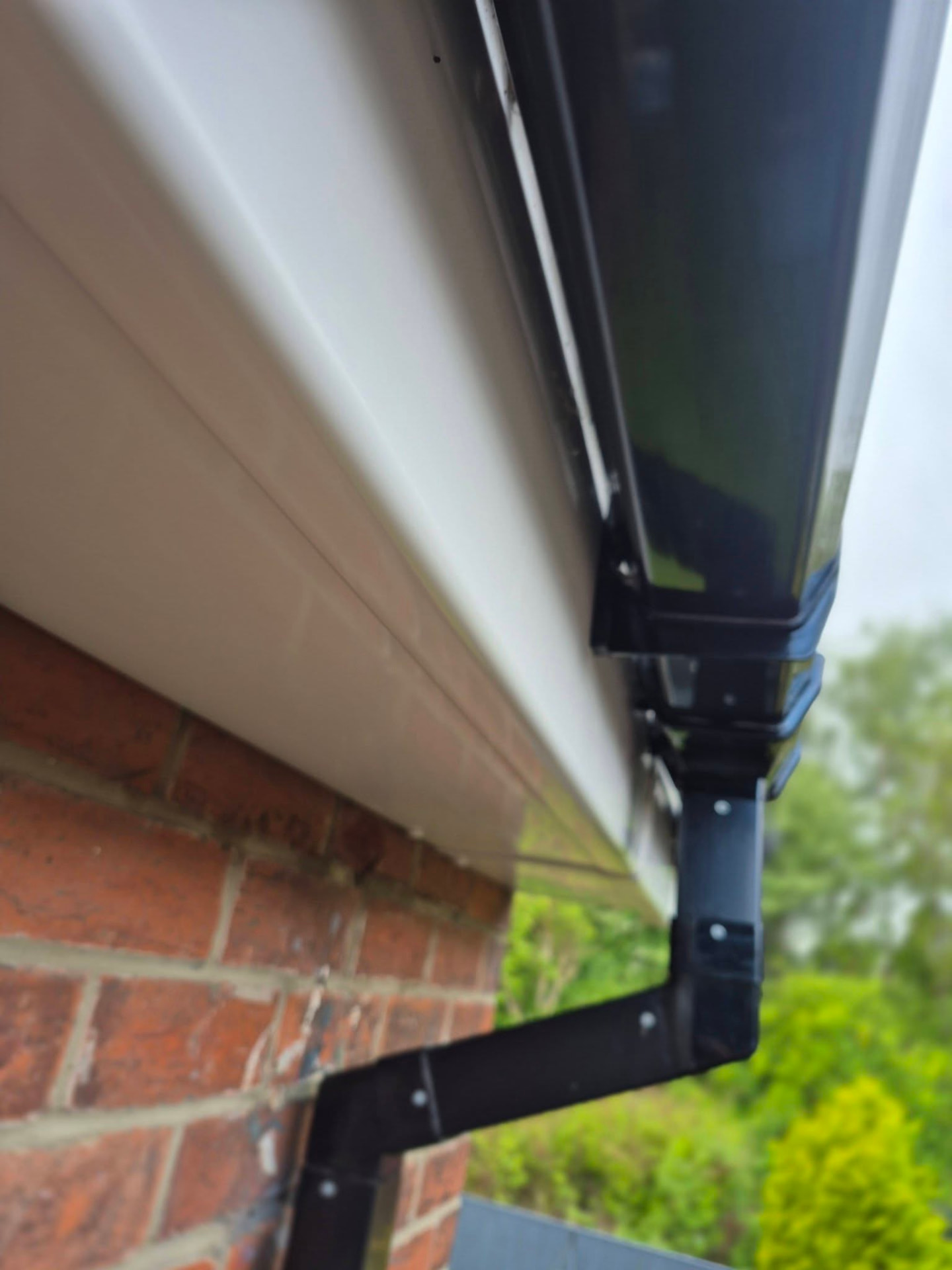 Black gutter and downpipe professionally finished against brickwork